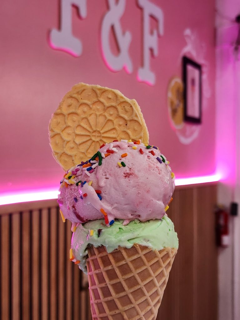 Double Scoops strawberry and pistachio nuts flavors in a waffle cone topped with sprinkles and homemade pizzelle